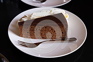 Piece of famous Sachertorte chocolate cake with apricot jam of Austrian origin served with whipped cream