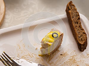 A piece of fish cake  lies on a plate with a slice of brown bread