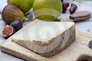 Piece of French cheese Tomme de Brebis made from sheep milk served as dessert with fresh figs and pears