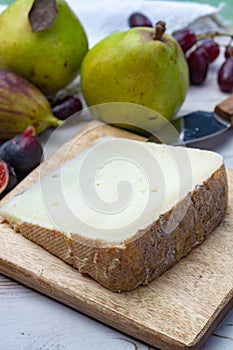 Piece of French cheese Tomme de Brebis made from sheep milk served as dessert with fresh figs and pears