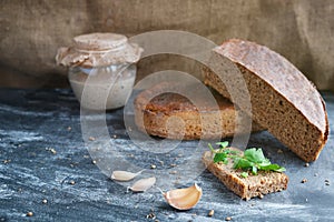 Piece fresh bread with parsley, onion chives, cloves garlic, sourdough in glass jar and loaf rye bread, spices on table