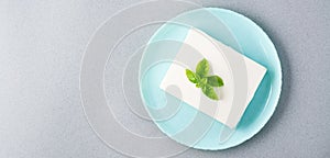 A piece of fresh feta cheese and basil leaves on a plate on the table. Ingredient for Greek salad. Top view. Web banner. Copy