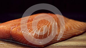 A piece of fresh, raw, red fish on a wooden brown cutting board, isolated on black background. Beautiful salmon fillet