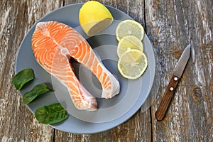 A piece of fresh salmon fish steak on a gray plate with spinach and lemon, on  a gray wooden background. Omega 3 vitamin, healthy