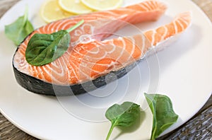 A piece of fresh salmon fish steak on a white plate with spinach and lemon, on  a gray wooden background. Omega 3 vitamin, healthy