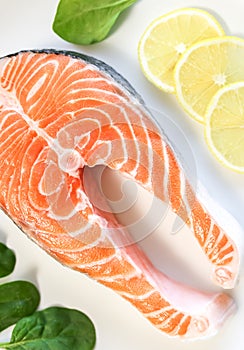 A piece of fresh salmon fish steak on a white plate with spinach and lemon, on  a gray wooden background. Omega 3 vitamin, healthy