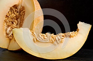 A piece of fresh sweet yellow melon sliced on wooden black table. Piece of raw organic melon on wooden dark background close up