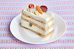 Piece of fruit yogurt cake with fresh strawberry, raspberry, peach, grapes and almonds on a white plate and pattern background.