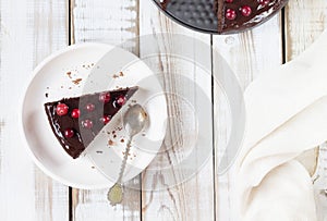 A piece of gluten-free brownie cake with chocolate icing, decorated with cranberries, on a white plate, on a light