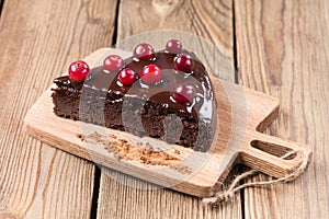 A piece of gluten-free cake in chocolate, decorated with cranberries, on the kitchen board, on a wooden background.