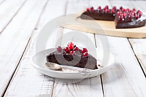 A piece of gluten-free chocolate cake decorated with cranberries, on a white plate, on a light wooden table.