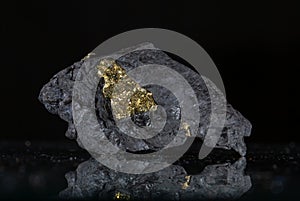 A piece of gold nugget on a black background with reflection.