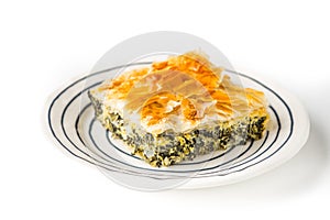 Piece of Greek pie spanakopita on the ceramic plate on the white background