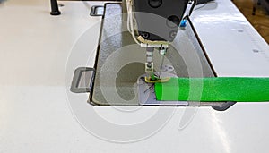 A piece of green cloth on a sewing machine. Steel needle with looper and presser foot close up