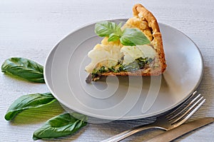 A piece of healthy cauliflower pie on the gray plate decorated with fresh basil leaves and vintage silver knife and fork