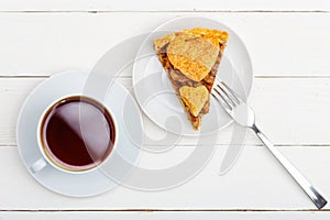 Piece of homemade apple pie with cinnamon and cup of tea on white wooden table
