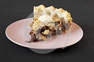 A piece of homemade Chocolate Walnut Derby Pie on a pink plate over black background, low angle view. Close-up photo