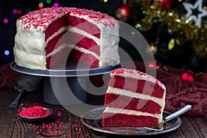 Piece of homemade red velvet cake with cream cheese frosting on a metal plate, low key photo with boke lights and christmas