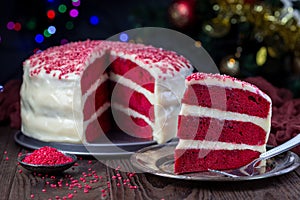 Piece of homemade red velvet cake with cream cheese frosting and red sugar decoration, low key photo with boke lights and