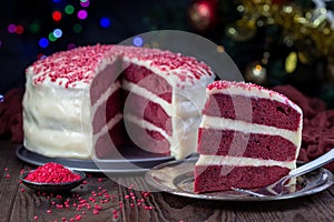 Piece of homemade red velvet cake with cream cheese frosting and red sugar decoration, low key photo with boke lights and