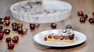 Piece of homemade yummy clafoutis pie with whole cherries on white plate