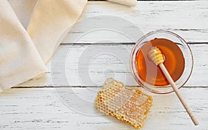 Piece of honeycomb organic fresh liquid honey in glass bowl with dipper on rustic background