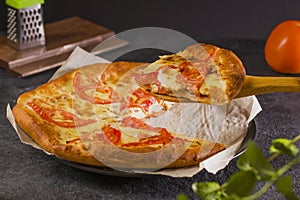 A piece of hot pizza with melting cheese on the table. Traditional Margherita pizza with tomatoes, basil and mozzarella cheese