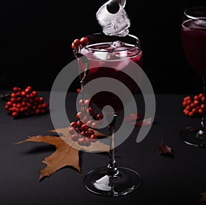 A piece of ice in the form of a skull falls into a glass with a red cocktail.