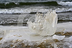 A piece of ice resembling a fist on the shore of a lake with waves