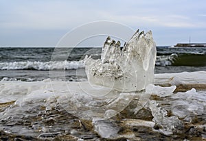 A piece of ice resembling a fist on the shore of a lake with waves