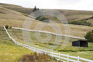 A piece of land enclosed with a white fence. Old wood shed. Countryside.