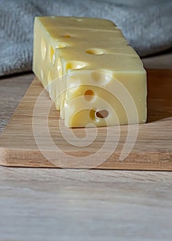 A piece of maasdam cheese on a wooden cutting board. Copy space