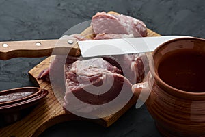 a piece of meat cut into pieces on a chopping board, a pot for chanakhi and a knife next to it
