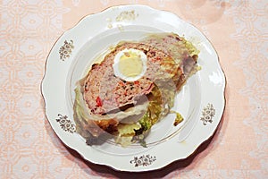 Piece of meatloaf in Savoy cabbage leaves in a beautiful vintage serving plate. half an egg in the center of the cut, a lot of