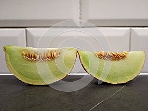 A piece of melon with seeds is on the table, cut melon white green. against the white brick wall