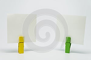 Piece of Memo paper clamped by yellow and green wooden clip with white background and selective focus
