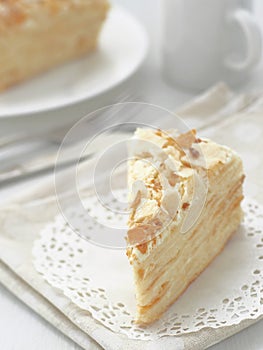 Piece of multi layered cake close-up. Mille feuille dessert. Crumbs decorated torte on white doily upon wooden table