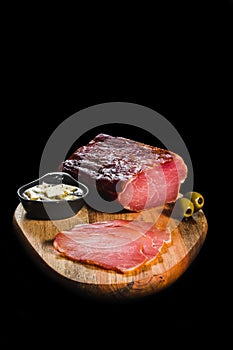 Piece od fresh dry meat with olives on wooden plate