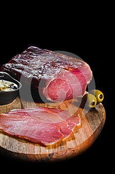 Piece od fresh dry meat with olives on wooden plate