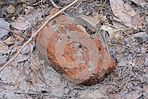 a piece of one old dirty brown red brick lies on gray sand