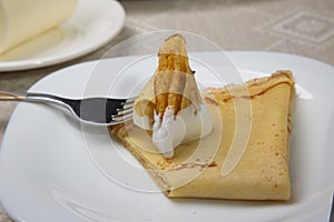 Piece of pancake in sour cream on a fork.