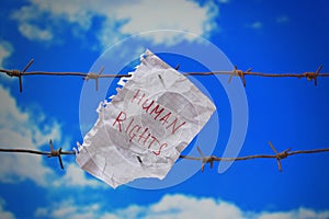 Piece of paper with human rights text on barbed wire on sky background