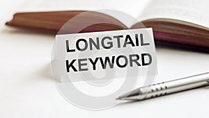 Piece of paper with text Longtail Keyword on the background of books, pens, on a white background