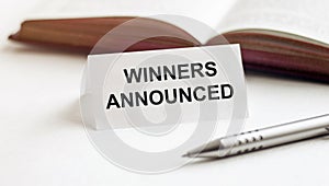 Piece of paper with text Winners Announced on the background of books, pens, on a white background