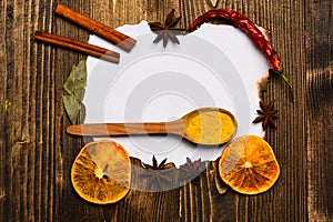 Piece of paper on wooden background. Culinary recipe concept. Spices, kitchen herbs lay around white paper. Cinnamon