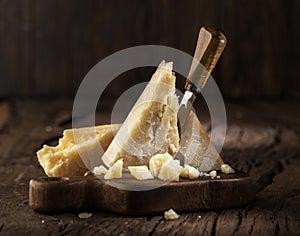 Piece of Parmesan cheese and cheese knife on the wooden board. Dark background