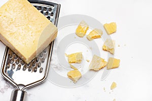 Piece of parmesan cheese on a cheese grater on a white and gray marble counter