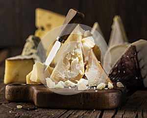 Piece of Parmesan cheese  on the wooden board. Assortment of different cheeses at the background
