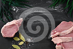 A piece of pork with cut pieces, sprinkled with flour on a black table. Bay leaf, black peppercorns, eucalyptus branches photo