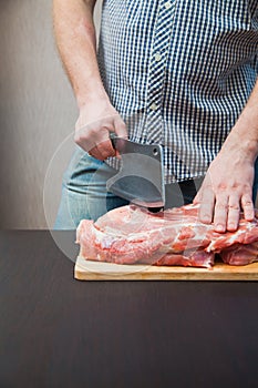 Piece of pork neck cutout on woodwn table. Man cutting meat